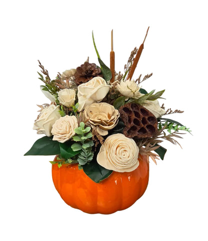 Ivory wood flower fall arrangement with greenery and natural accents in an orange pumpkin planter.